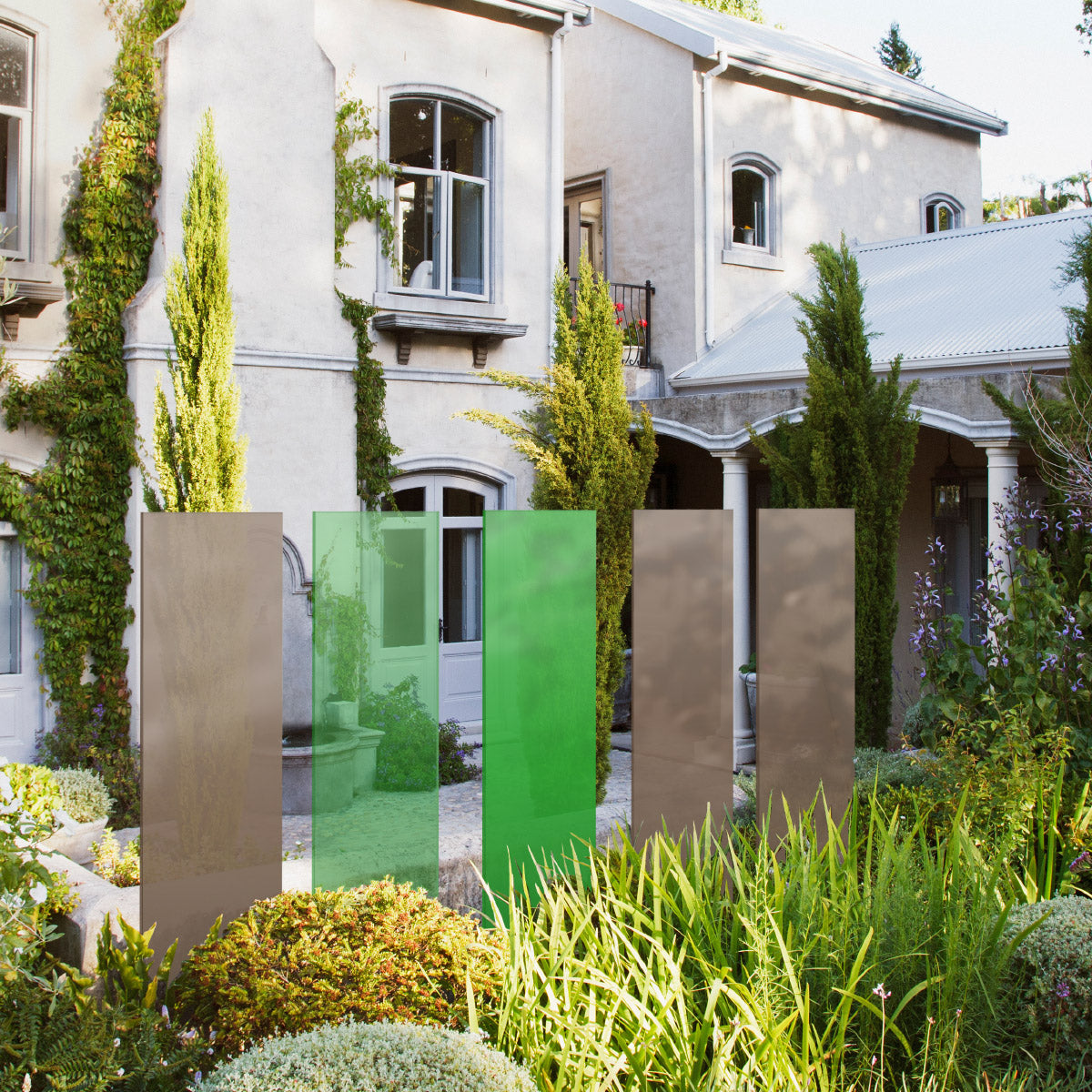 Eine KNUMOX Kollektion mit 2 grünen und 3 beigen Glaselementen steht in einem Garten vor einem Haus mit Säulen.