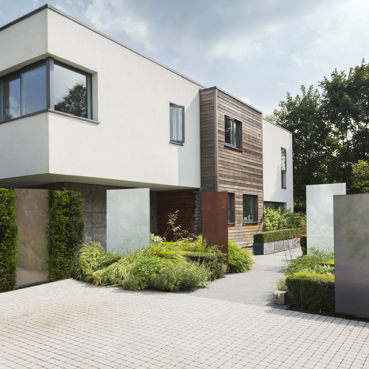 Fünf  KNUMOX Glasdesign Elemente stehen vor einem modernen Haus. Zwei der Elemente sind weiß, zwei sind beige-braun und eines ist grau.