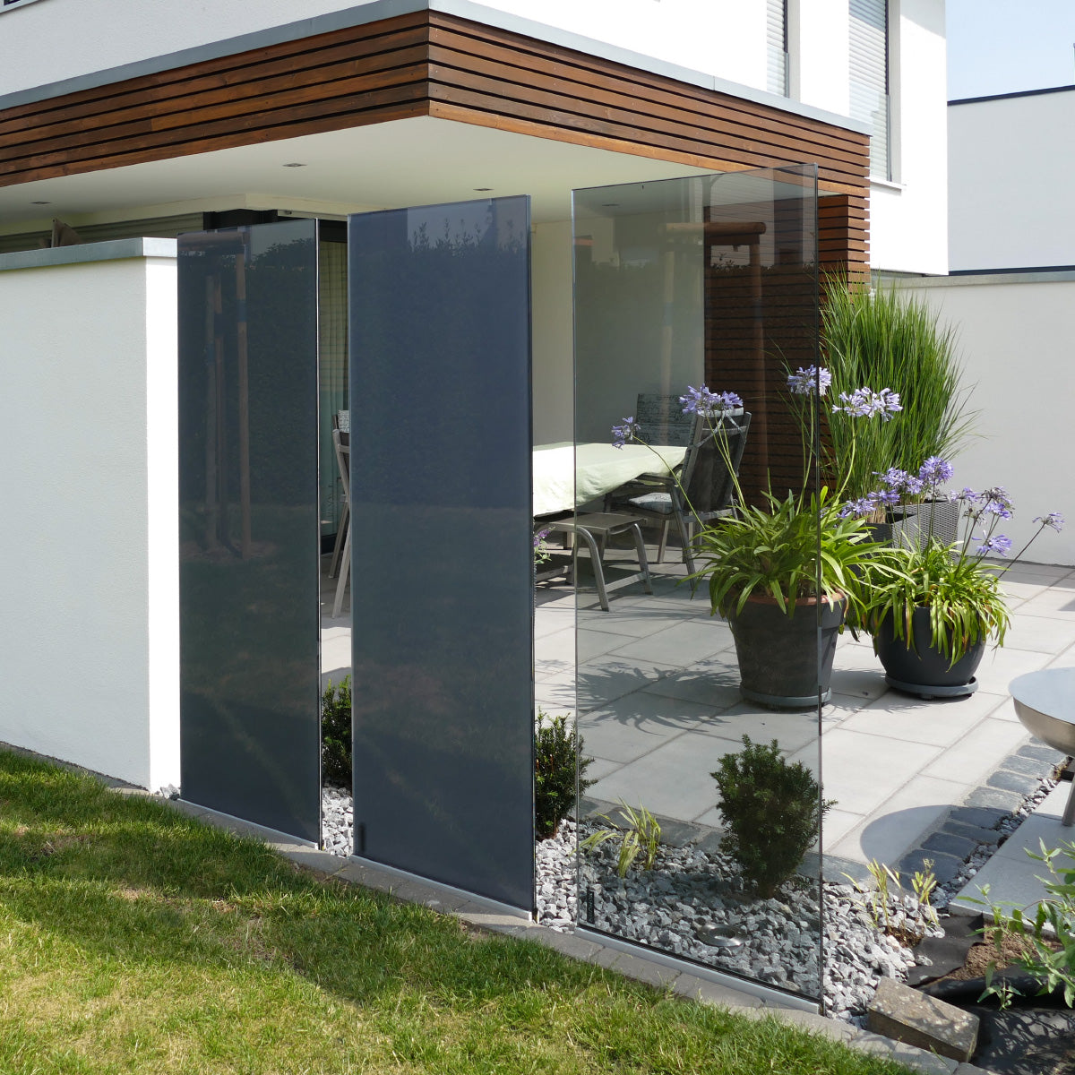 Drei graue Glasdesignelemente stehen in drei unterschiedlichen Durchlässigkeiten vor einer Terrasse.