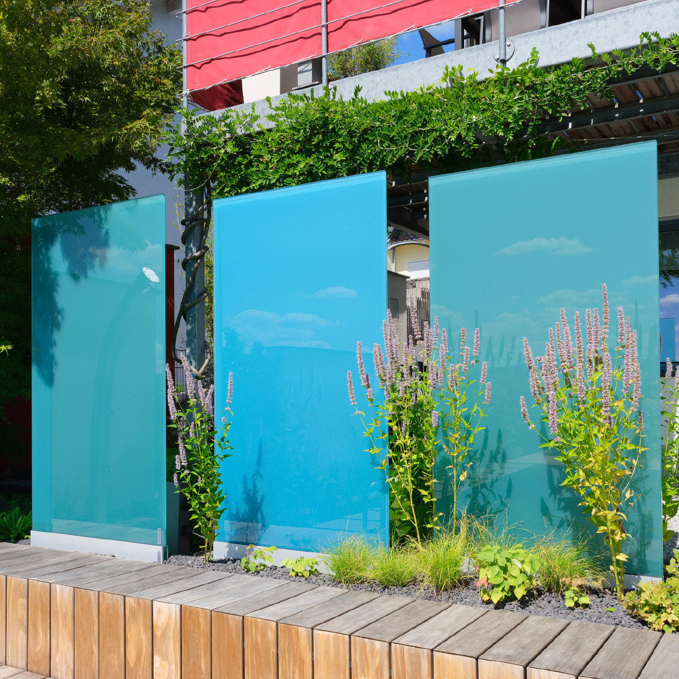 Drei blaue Sichtschutz Designelemente aus Glas stehen in einem Garten.