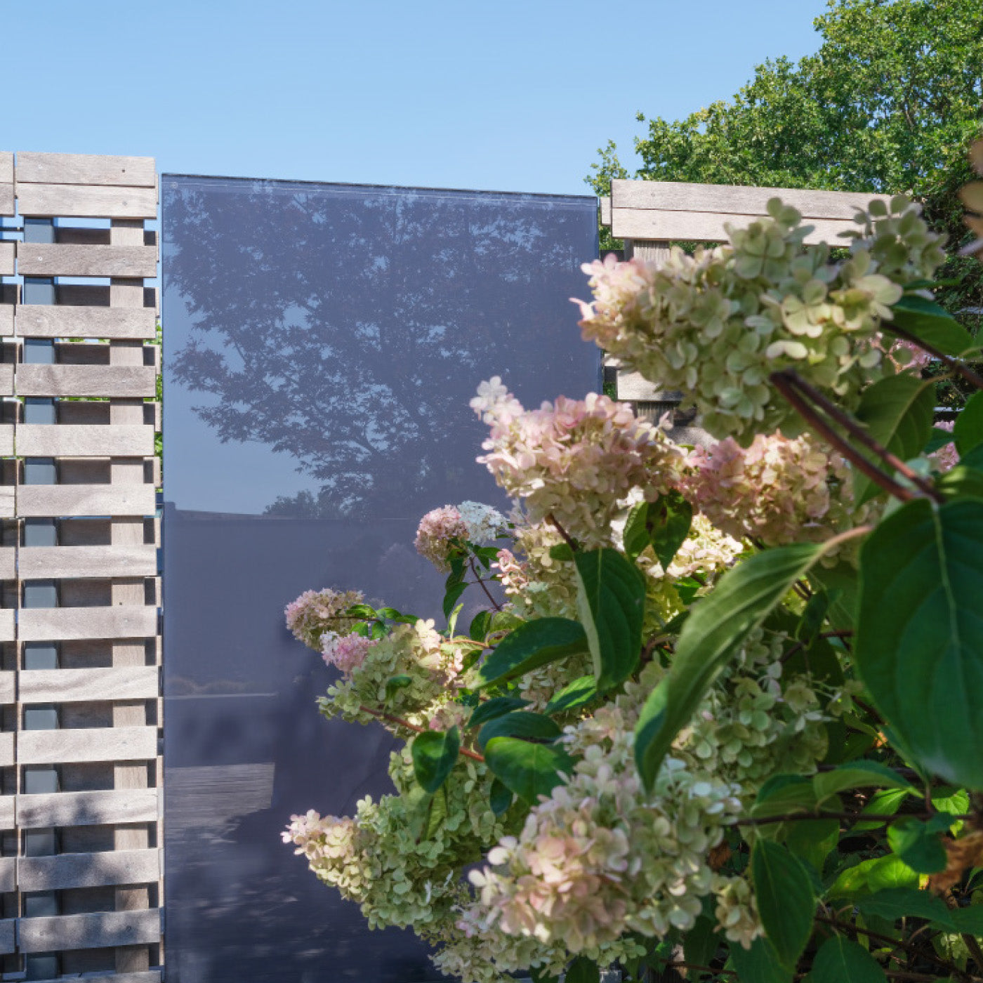 Graues Sichtschutz Designelement aus Glas als Teil eines Zaunes, im Vordergrund sind Stauden zu sehen.