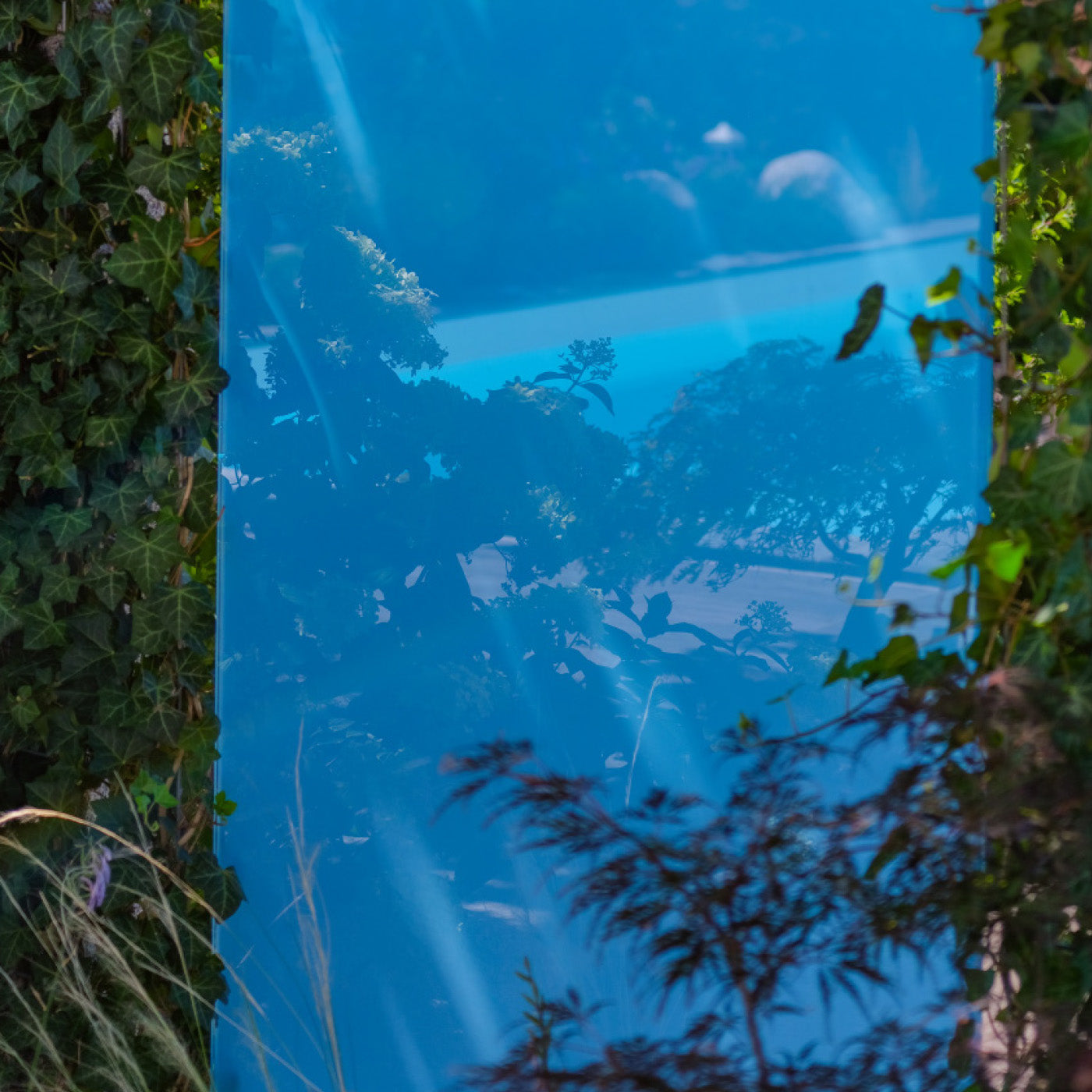Blaues Sichtschutz Designelement aus Glas von KNUMOX, in dem Spiegelungen eines Pools zu sehen sind.