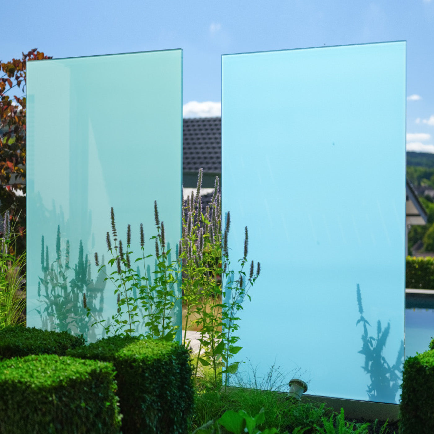 Zwei blaue Sichtschutz Designelemente aus Glas, die von Sonnenlicht angestrahlt werden und Schatten von Pflanzen zu sehen sind.