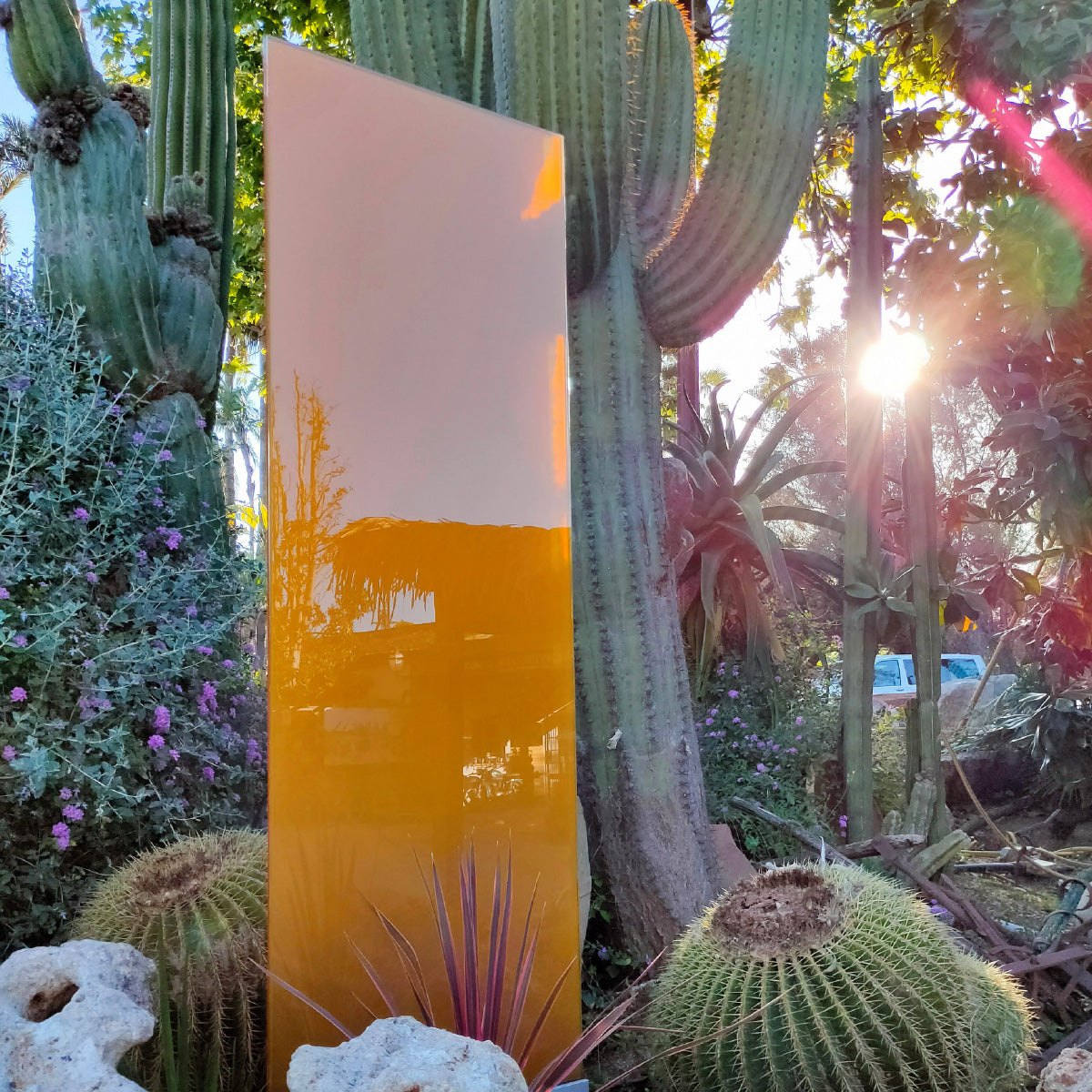 Das Glaselement mit orangener Farbe steht zwischen Kakteen im Aussenbereich von "Jardins de Tramuntana" in Mallorca. 